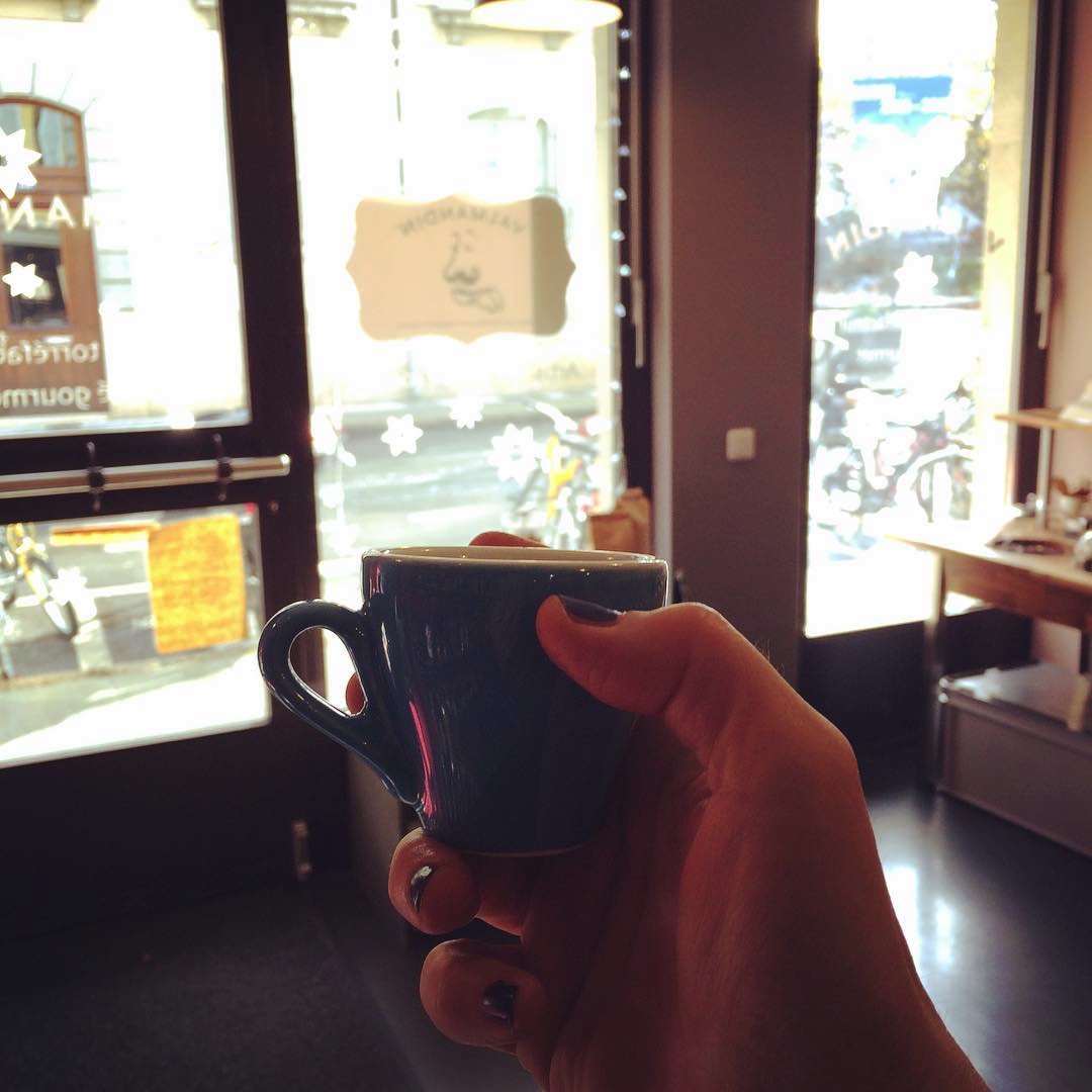 A hand holding a cup of delicious Valmandin espresso against a light flooded shop window.