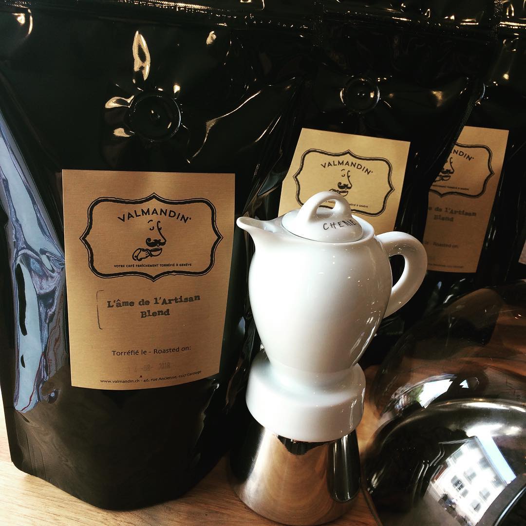 Une cafetière italienne en porcelaine blanche devant des sachets avec des cafés gourmet Valmandin. Préparer le meilleur café pour savourer avec des amis.